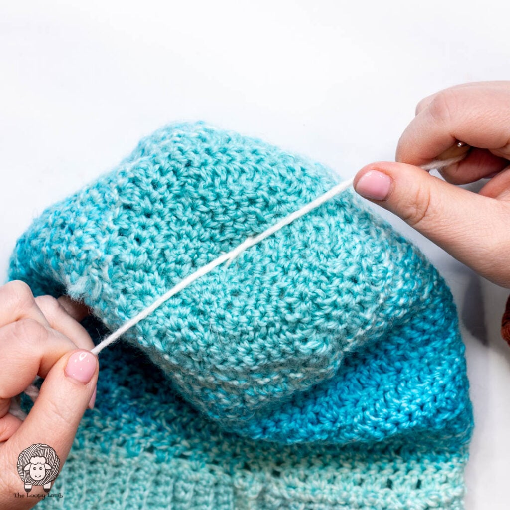 step 5 of how to attach a yarn pom pom to a hat: tying a knot on the inside of the hat.