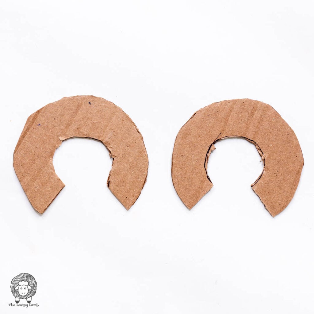 two c-shaped cardboard cutouts to make a yarn pom pom maker on a white background