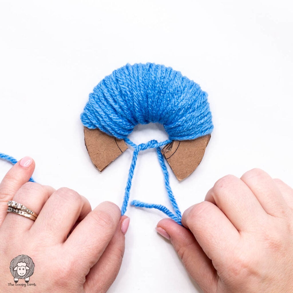hands starting to tie a knot in the yarn strands that were placed between the cardboard template pieces