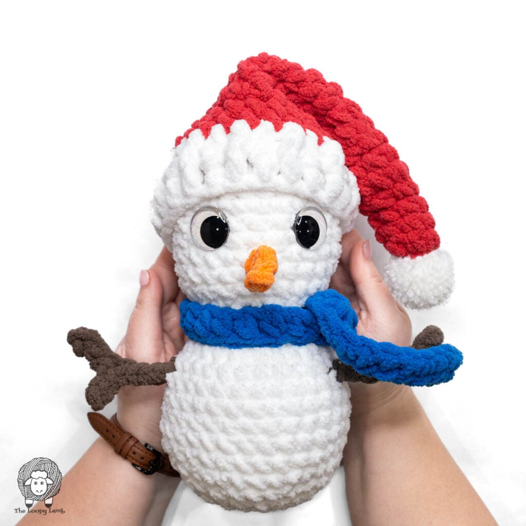 hands holding a crochet snowman wearing a mini crochet santa hat