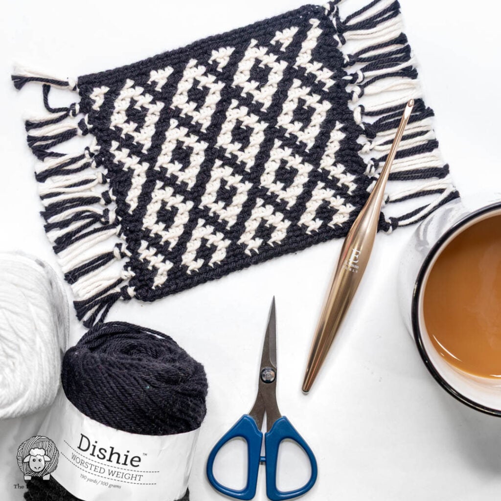 Dazzling Diamonds easy tapestry crochet coaster on a white background with crochet hook, coffee and dishie yarn