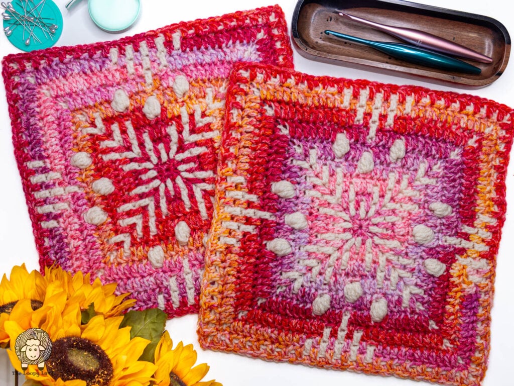 two 12" mosaic granny squares on a white background next to some sunflowers and furls crochet hooks