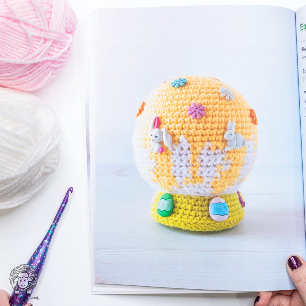 Easter-themed crochet snow globe shown in the book, next to some yarn and a crochet hook