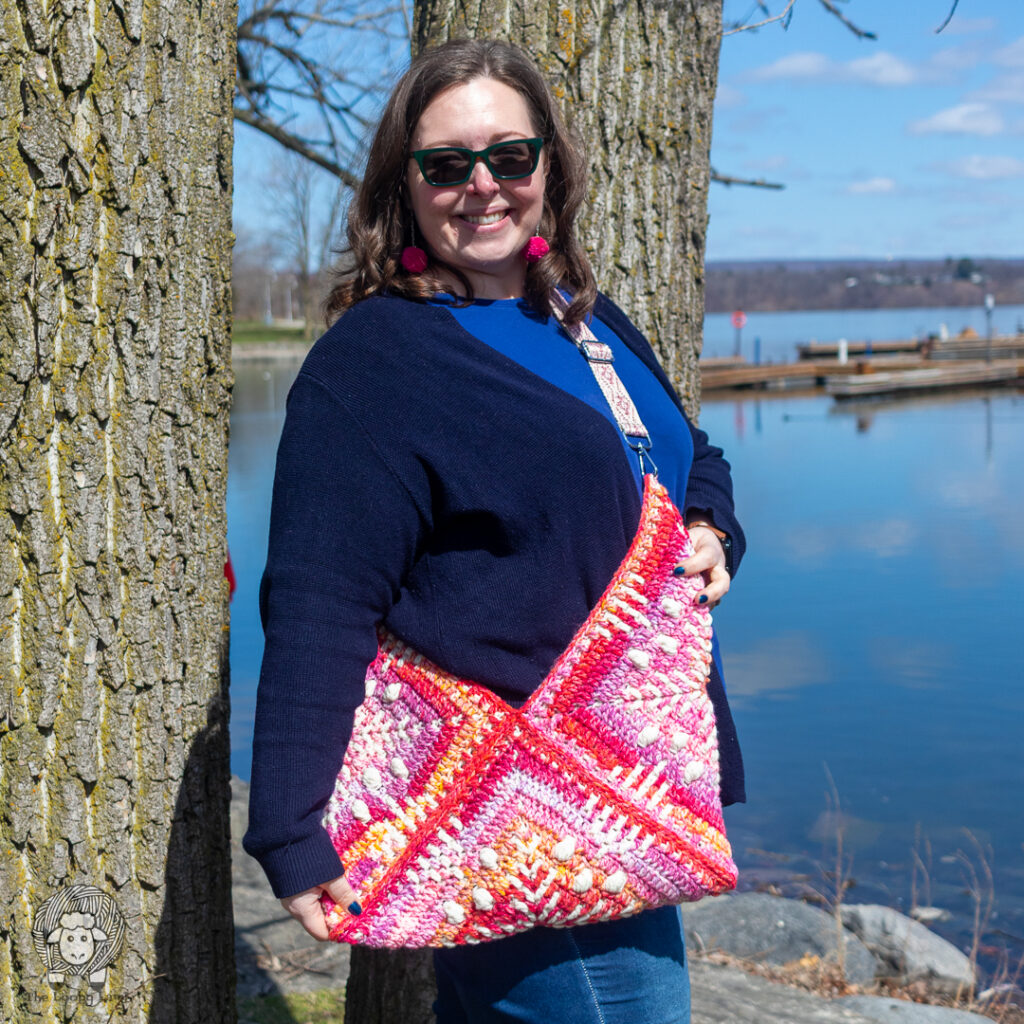 smiling woman wearing a large crochet granny square tote bag