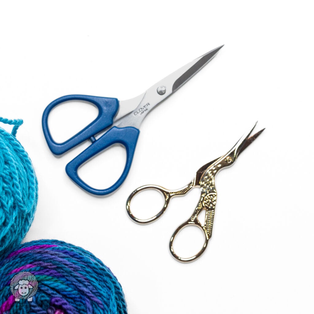 two different pairs of scissors on a white background next to some yarn