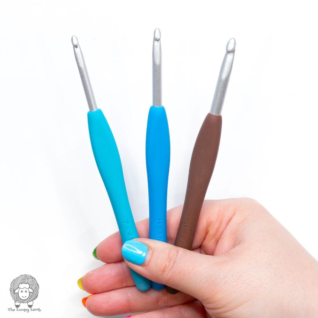 good crochet hooks are essentaial crochet tools beginners should have. hand holds 3 different sized crochet hooks against a white background