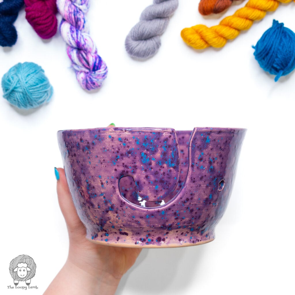 hand holding a ceramic yarn bowl under various colored yarn minis