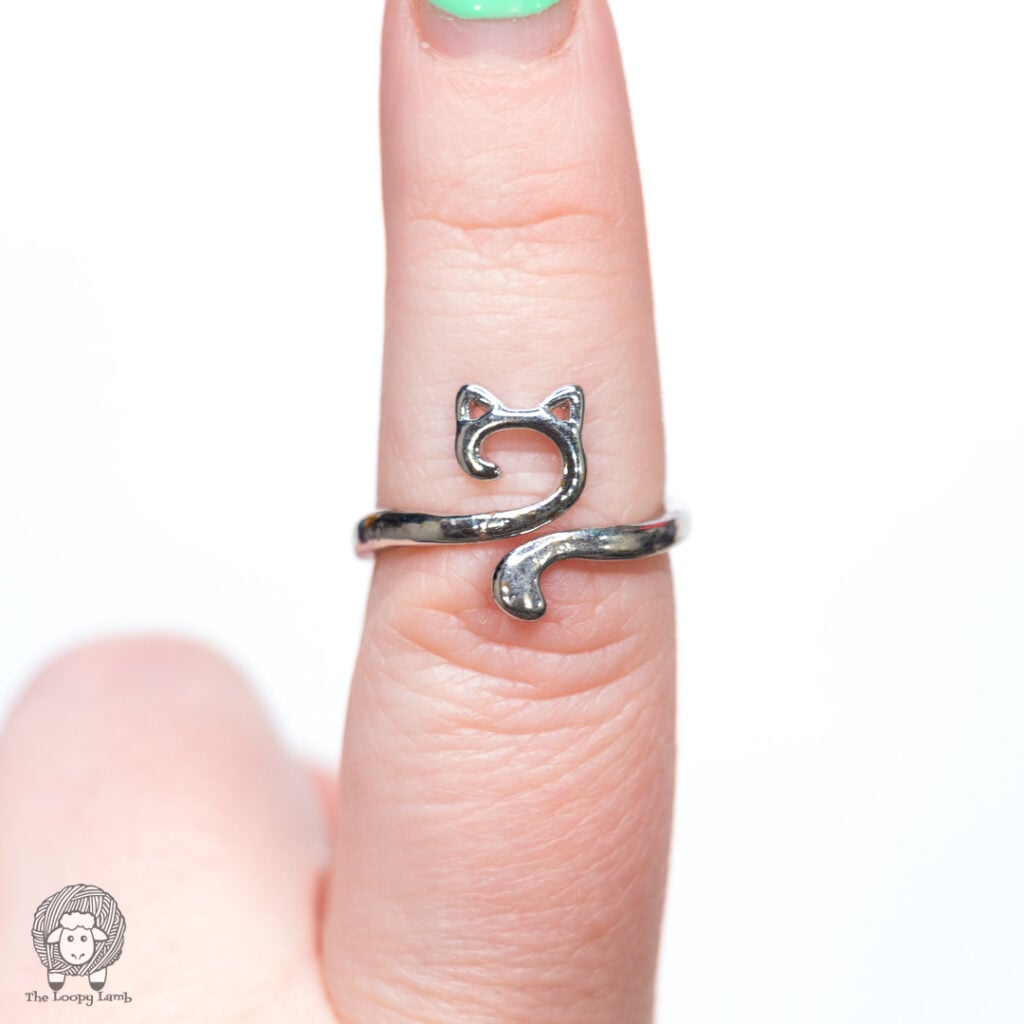 cat-themed crochet tension ring on an index finger against a white background