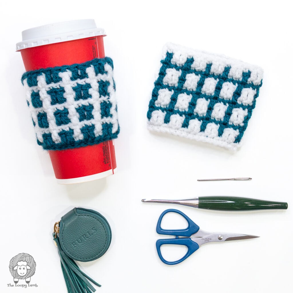 mosaic crochet cup cozy on a cup and one on a white background next to a crochet hook, scissors, tapestry needle and tape measure